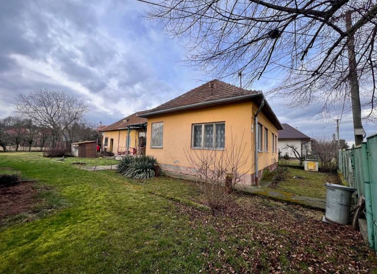 A family house in Komjatice with a front garden surrounded by trees and lawn.