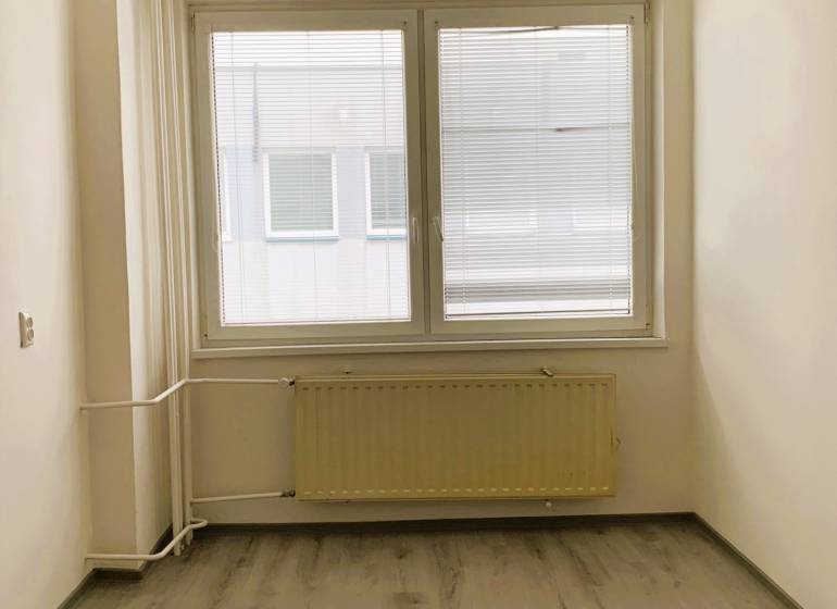 An office with a window, a wooden-patterned floor, and a radiator.