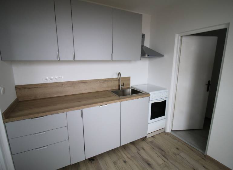 A kitchen in a 3-room apartment with a wooden decor floor and a simple kitchen unit.