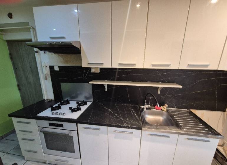 A kitchen in a 3-room apartment with an elegant white unit and black tiles.