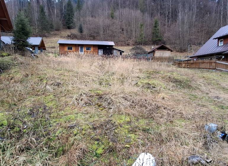 A plot for residential use in Oščadnica, with a wooden house and a forest backdrop.