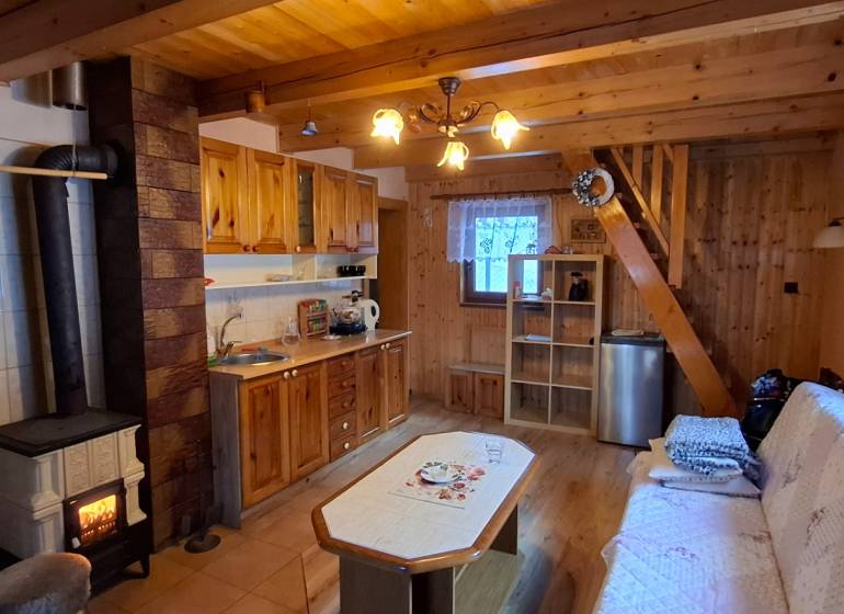 A wooden interior of a cabin with a fireplace, kitchen, and floor with wooden decor.