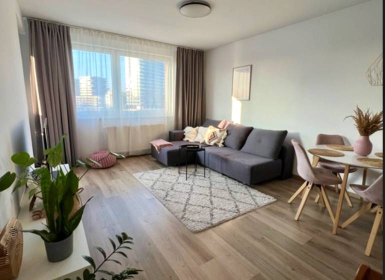 Living room in a two-room apartment with a sofa, table, and wooden decor flooring.