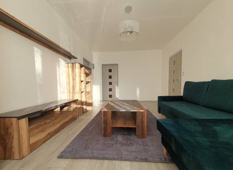 Living room in a three-room apartment with a sofa, wardrobe, and table on a wooden decor floor.