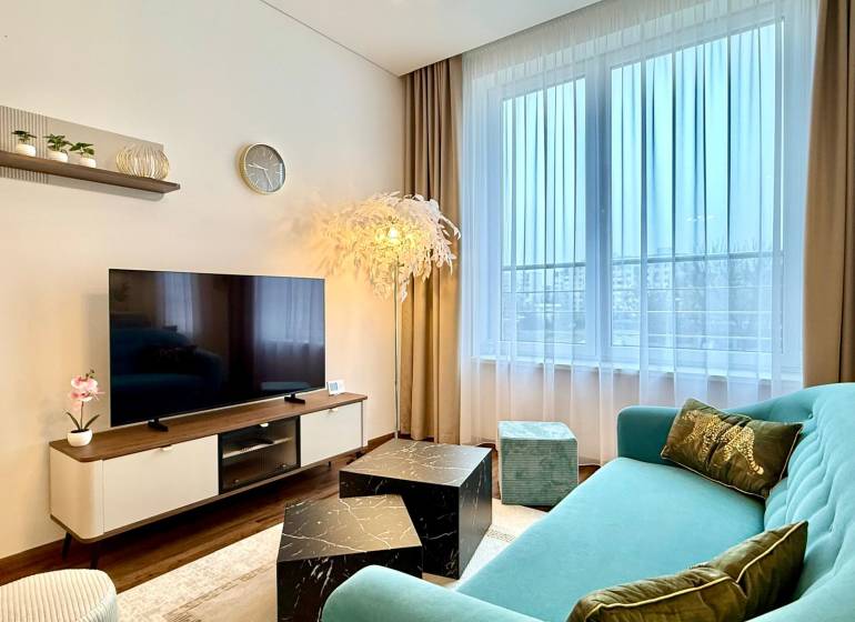 Living room in a two-room apartment with a wooden decor floor, a comfortable sofa, and a television.