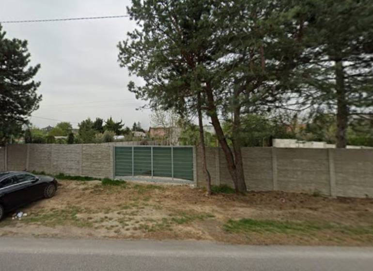 Commercial plots on Dukelská in Bernolákovo with a concrete fence and access road.