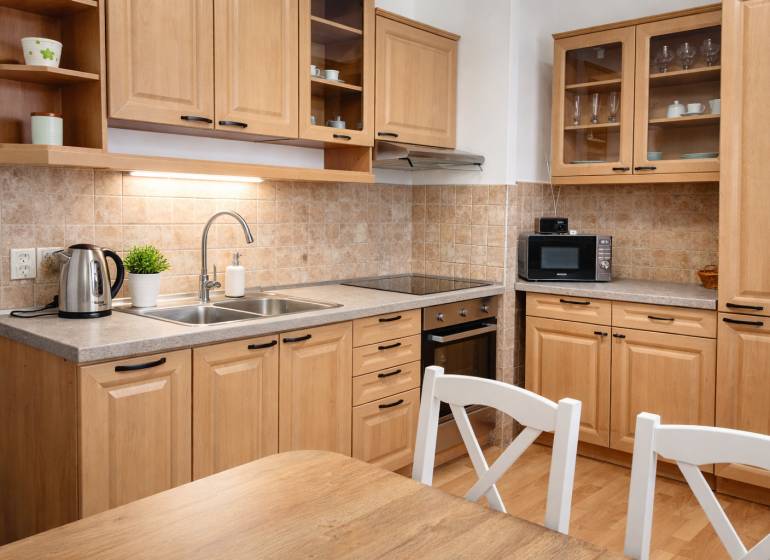 A kitchen in a 3-room apartment with wooden decor, kitchen cabinets, appliances, and a table.