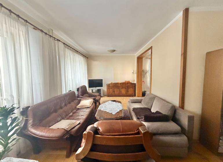Living room in a family house with a wooden decor floor, a sofa, and curtains.