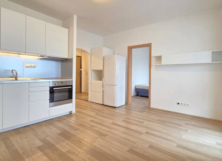 A kitchen in a studio apartment with white cabinets and a wooden decor floor.