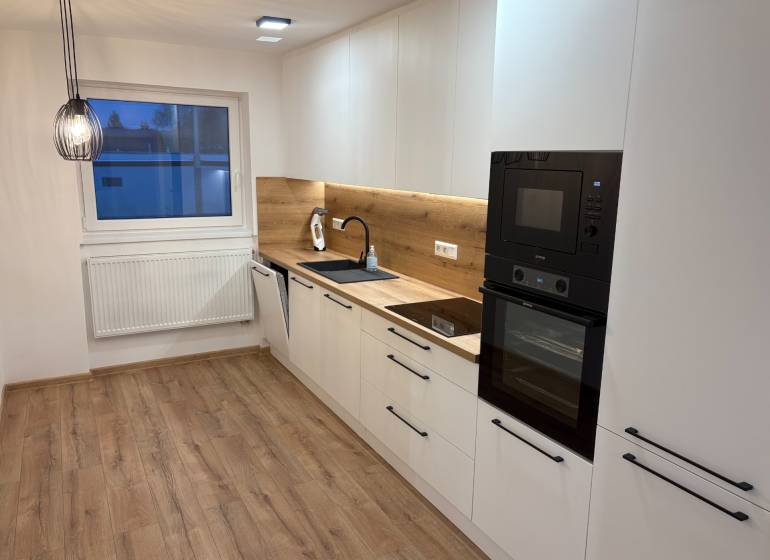 A kitchen in a 3-room apartment with white cabinets, wood-patterned flooring, and a built-in oven.