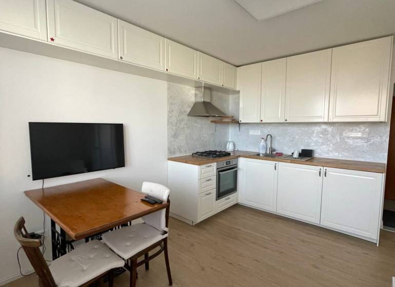 A kitchen in a studio apartment with a wood-patterned floor and a dining table.