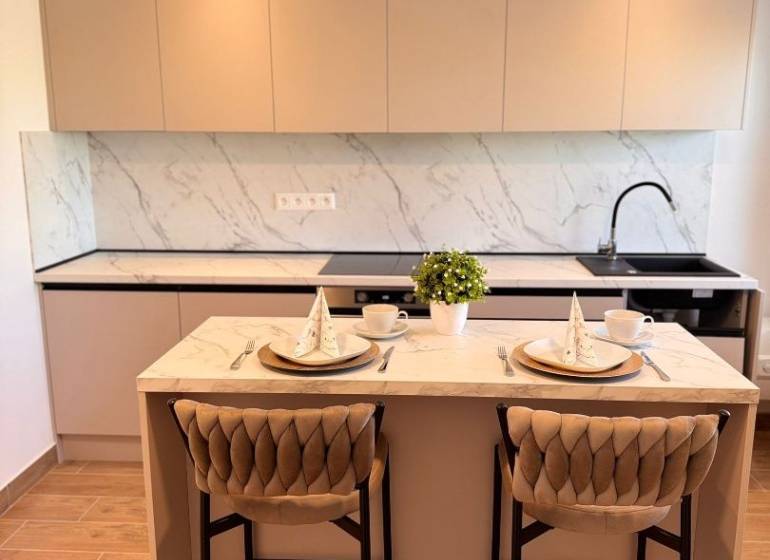 A kitchen in a 2-room apartment with a white marble countertop and a wooden decor floor.