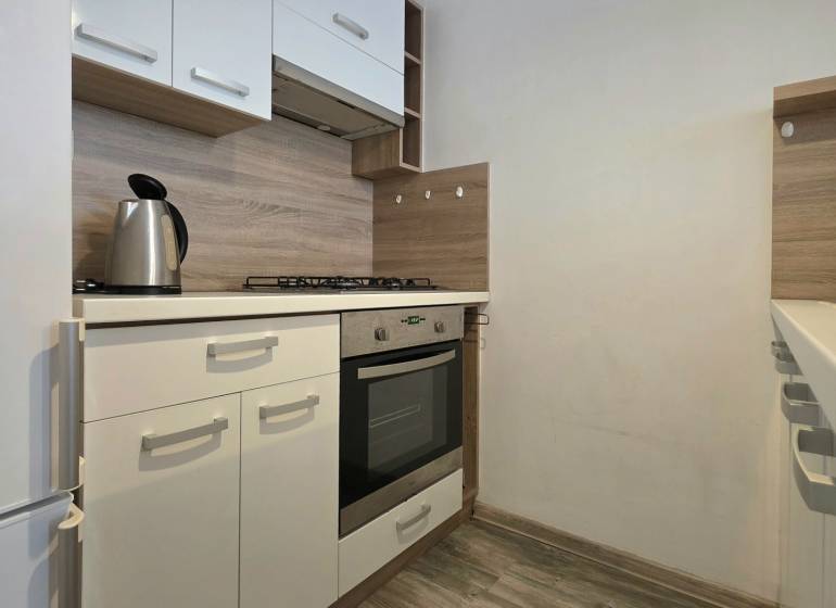A kitchen in a 2-room apartment with white cabinets and a wood-patterned floor.