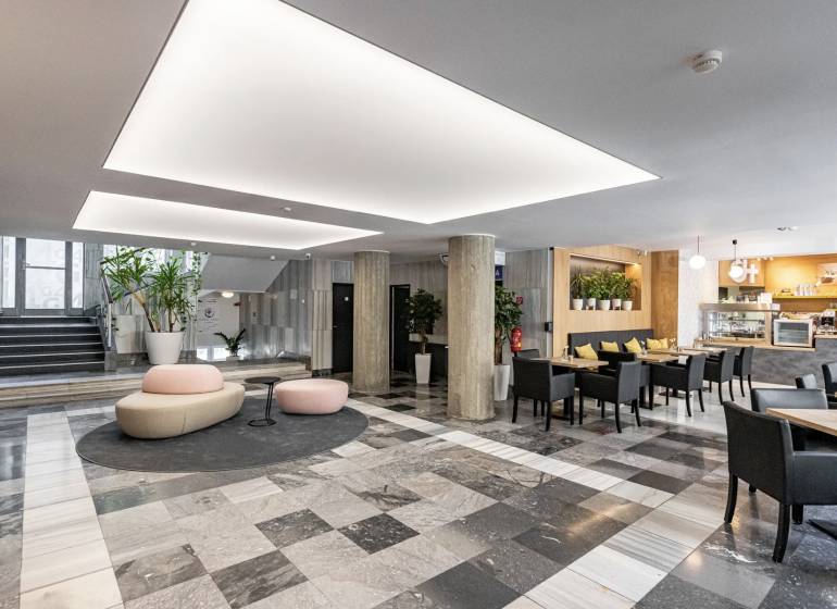 Offices with black and white flooring, columns, seating, and a café in the interior.