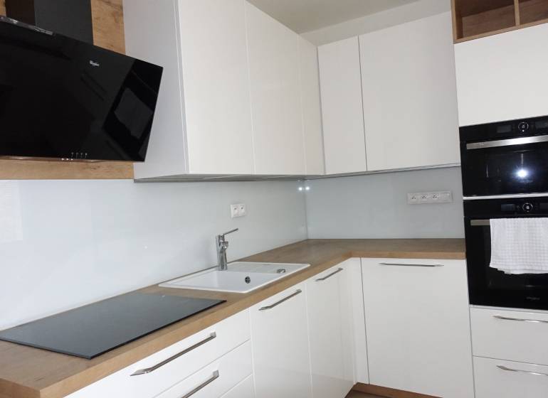 A kitchen with white cabinets and appliances, complemented by a wood-patterned floor in a three-room apartment.