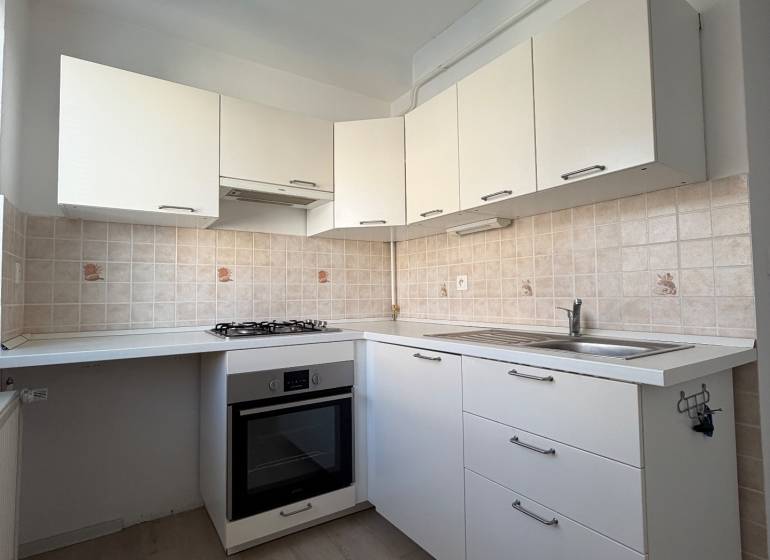 A kitchen in a studio apartment with white cabinets, a cooktop, and a wooden decor floor.