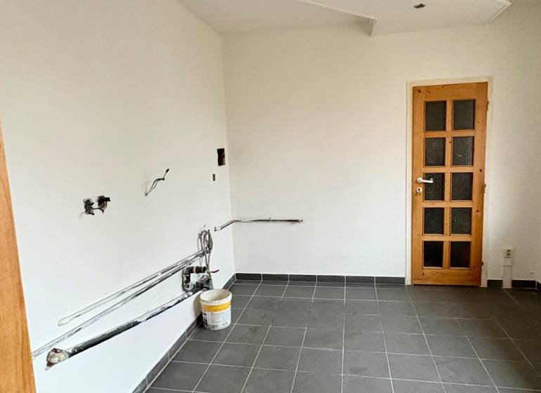 An empty room in a two-room apartment, dark tiled floor, white walls, wooden doors.