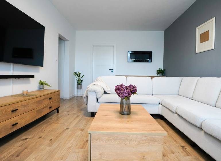 Living room in a 3-room apartment with a white couch, wood-patterned flooring, and decorations.