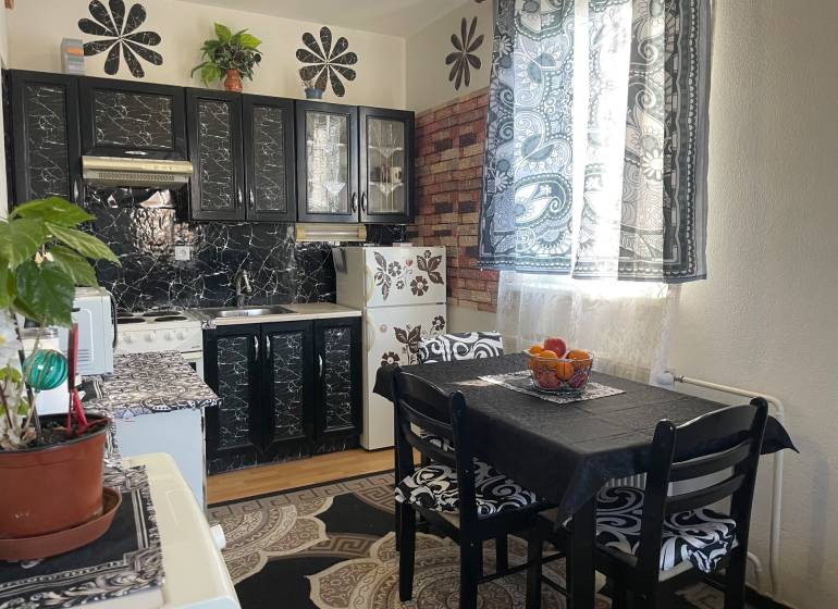 A kitchen with tables, black cabinets, and patterned curtains in a studio apartment.