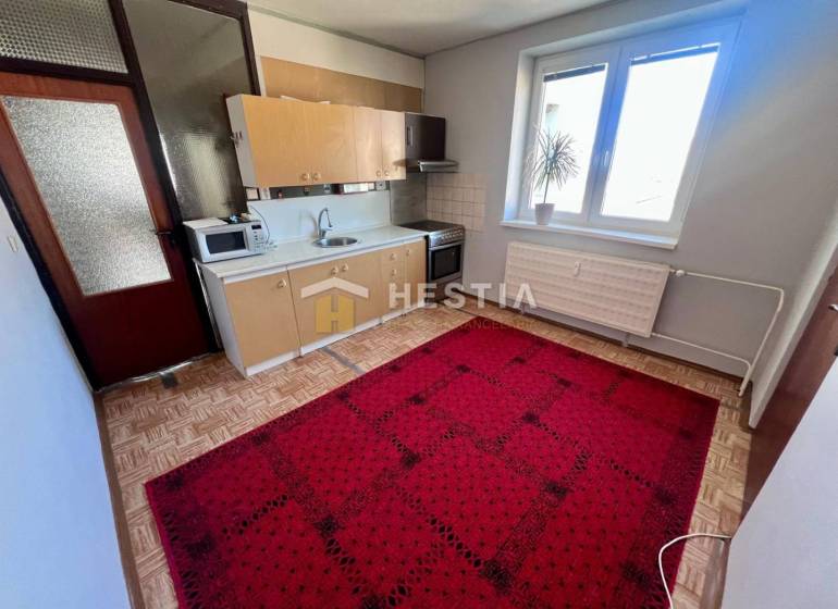 A kitchen in a 3-room apartment with a wooden decor floor and a red carpet.