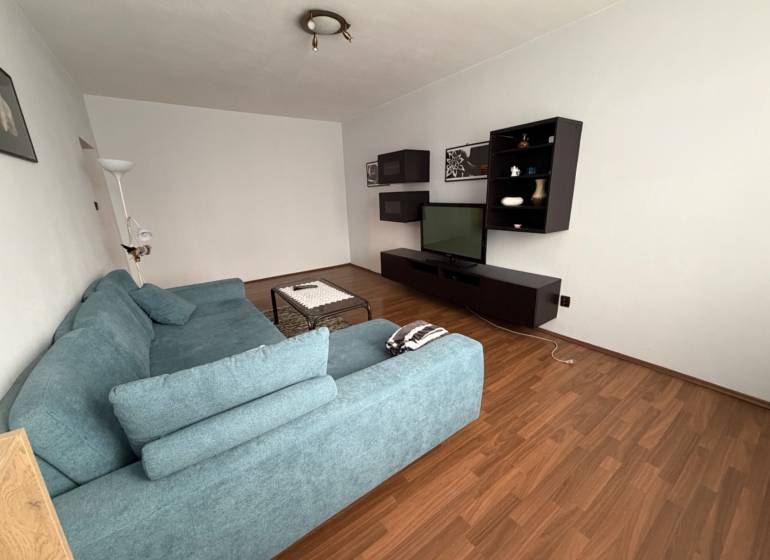 Living room with a TV, blue sofa, and wood-patterned flooring in a 3-room apartment.