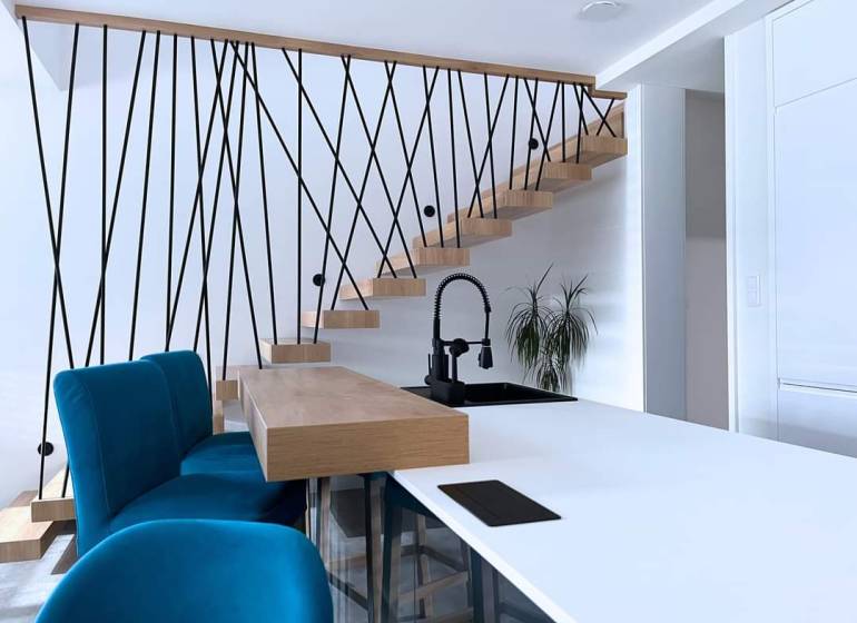 The interior of a family house with a staircase, blue chairs, and a kitchen counter.