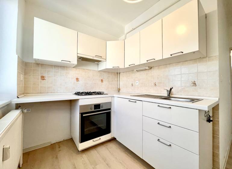 A kitchen in a studio apartment with white cabinets and a wooden decor floor.