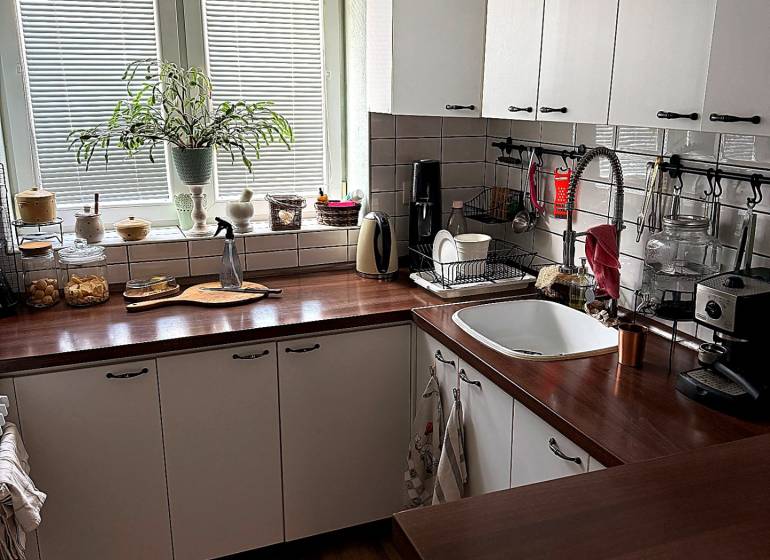 The kitchen of a two-room apartment with a wooden decor floor and white cabinets.