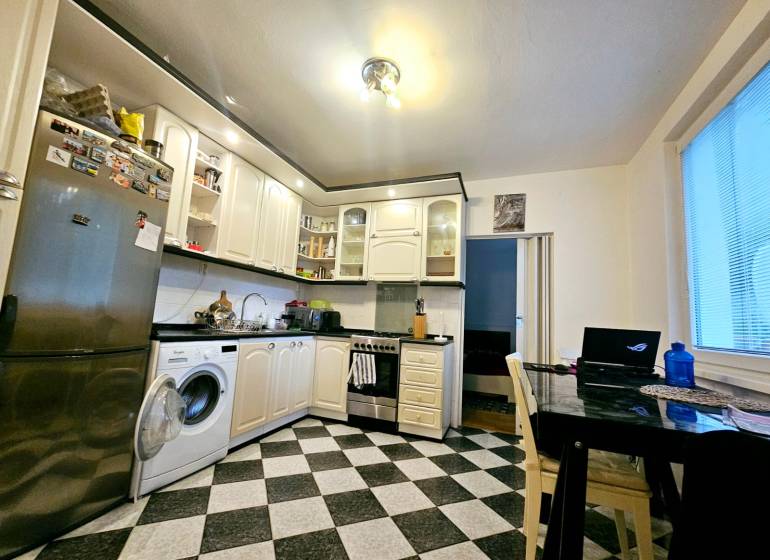 A kitchen in a 3-room apartment with tiles, equipped with appliances and a dining table.