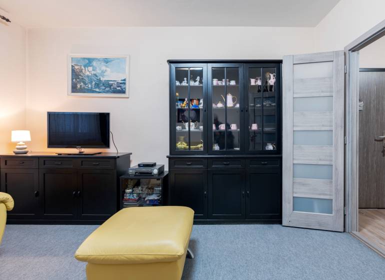 Living room in a 4-room apartment with dark furniture, a television, and a display cabinet.