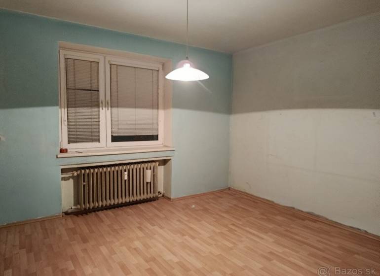 A room with a wooden decor floor, a radiator, and a window with blinds in a 2-room apartment.
