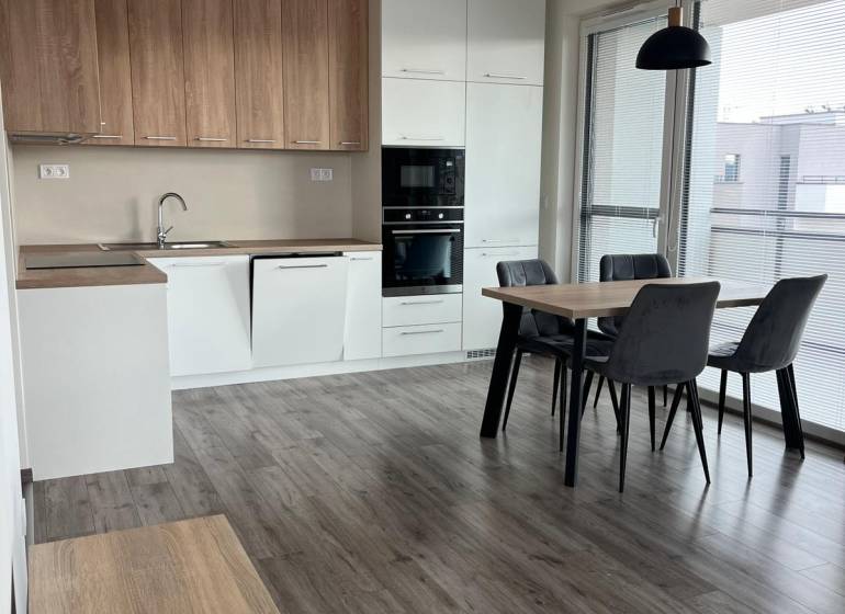 A kitchen with built-in appliances and a dining table in a 3-room apartment, floor with a wooden decor.