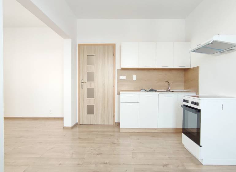 A kitchen in a 2-room apartment with white cabinets, a stove, and a wooden decor floor.