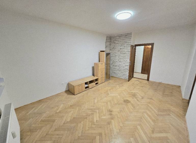 A bright room in a two-room apartment with a wood-decorated floor and furniture.