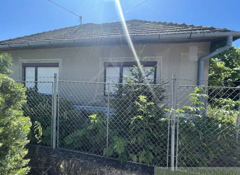 A family house in Tvrdošovce with a fence and greenery, under a clear sunny sky.