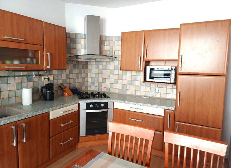 A kitchen in a 3-room apartment with a wood-patterned floor and kitchen cabinets.