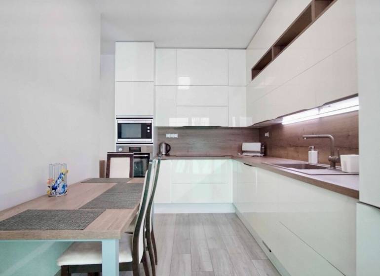 A kitchen in a 3-room apartment with a wooden decor floor and light furniture.