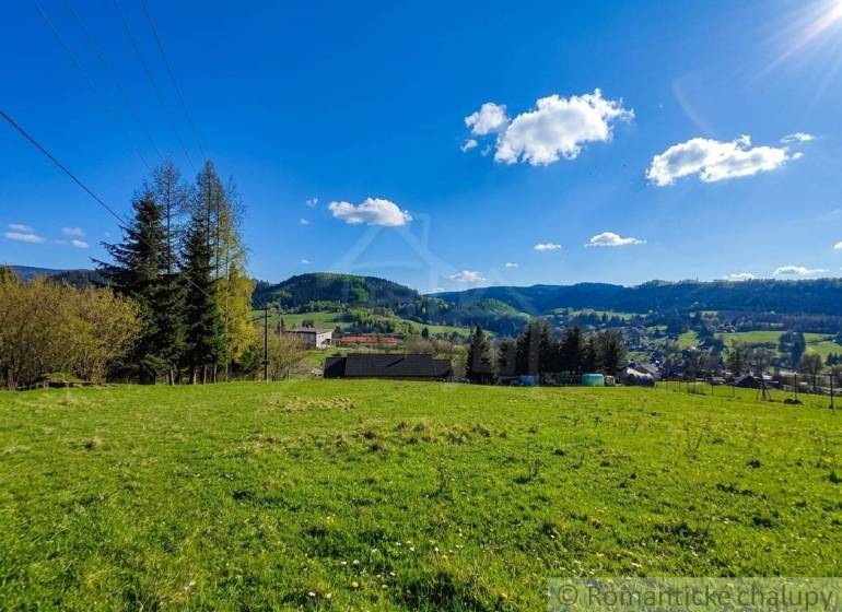 A landscape with a meadow and trees in the Gardens of Ľubietová, surrounded by hills and a blue sky.