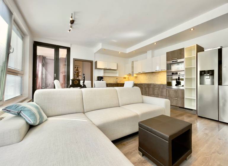Living room of a three-room apartment with a white sofa and a kitchen unit.