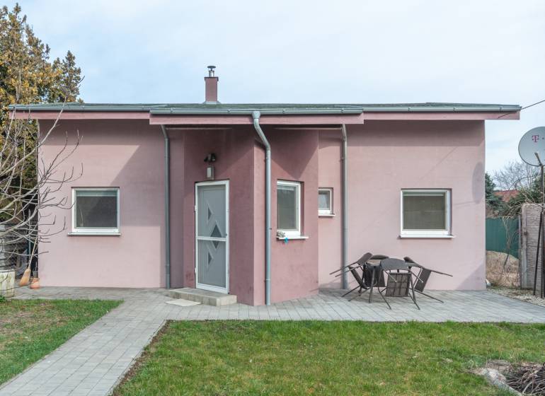 A family house in Šurany with a pink facade and a garden seating area on a paved walkway.
