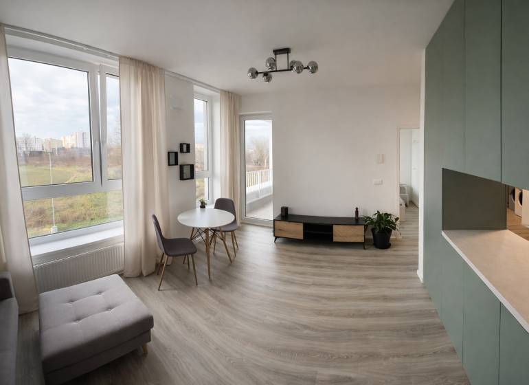 Living room in a two-room apartment with a wooden decor floor and large windows.