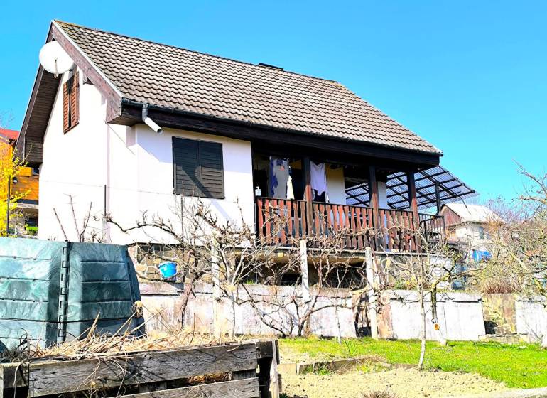 A cottage in Partizánske with a garden and terrace, surrounded by greenery and a blue sky.