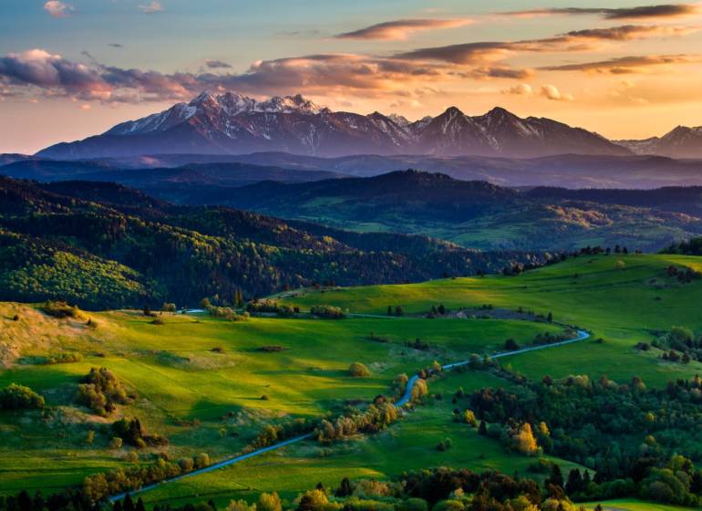 A landscape with agricultural and forest land surrounded by mountains in the Hrabkova area at sunset.