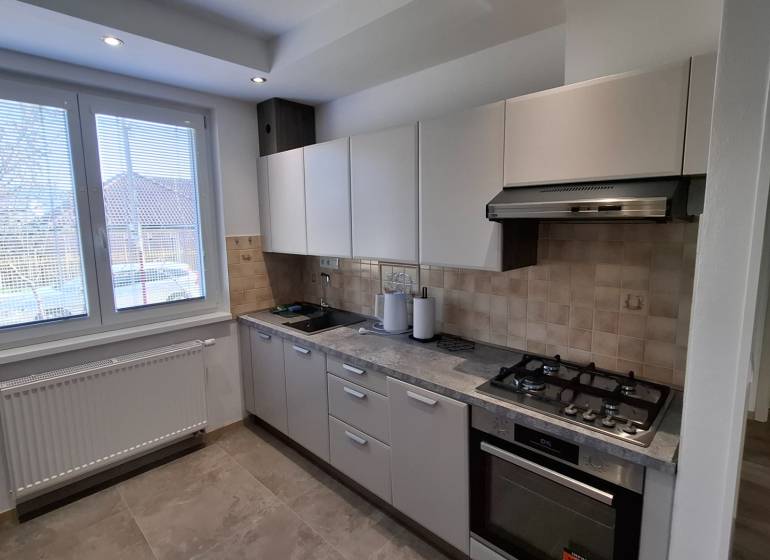 Kitchen area of a 2-room apartment with a gas stove, white cabinets, and a large window.