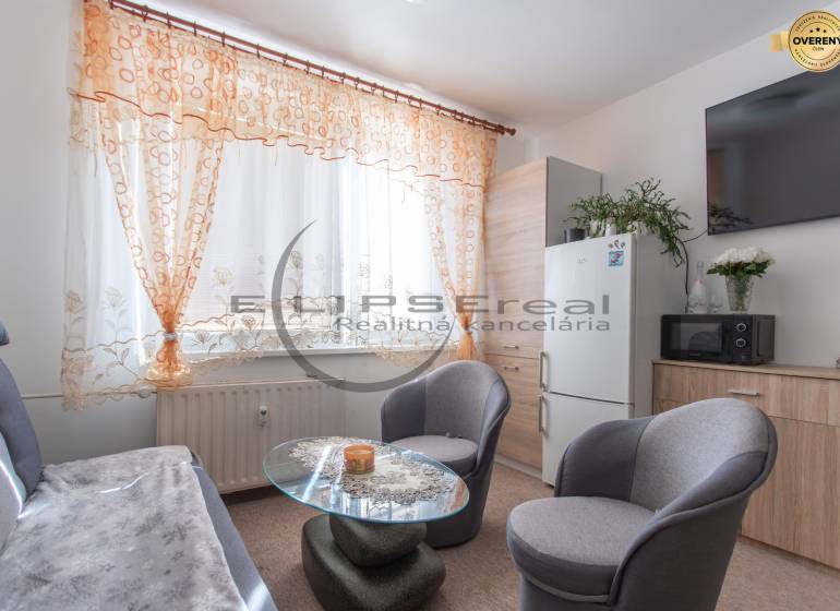 Living area of a studio apartment with a sofa, table, and colorful curtains.