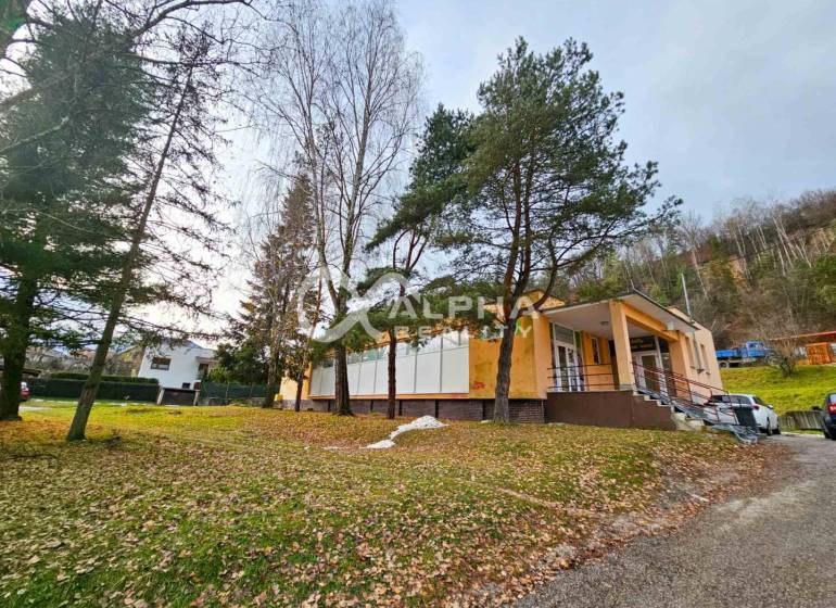 A building in Helcmanovce surrounded by trees, with a staircase leading to the entrance.