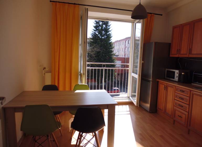 A kitchen in a studio apartment with furniture, yellow curtains, and a wooden decor floor.