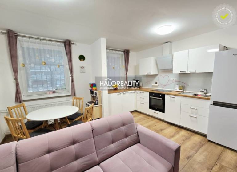Living room with a pink sofa, kitchen, and wooden decor flooring in a three-room apartment.