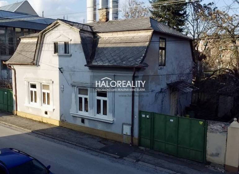A family house in Rimavská Sobota with a classic roof design, a large gate, and neighboring buildings.