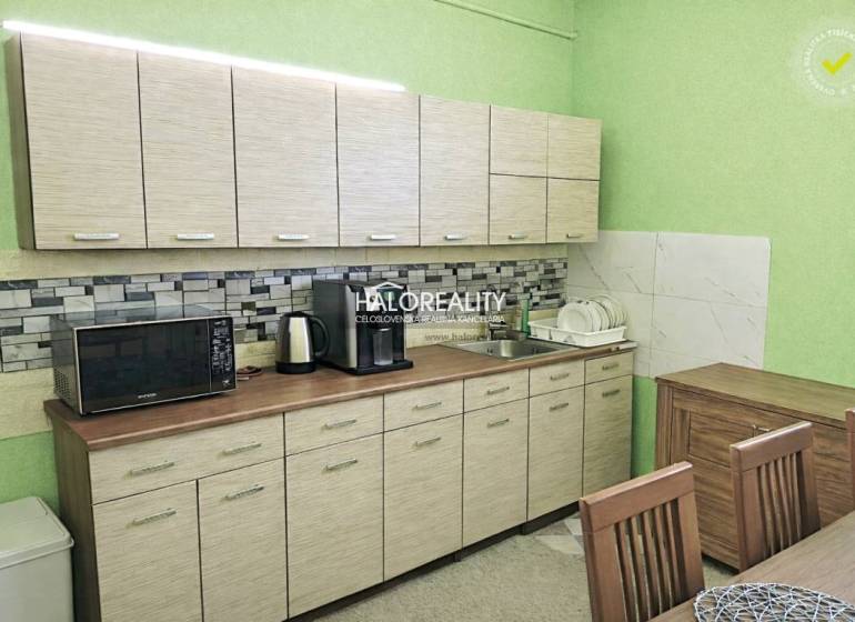 A kitchen in a family house with light furniture, a microwave, and dishes by the sink.
